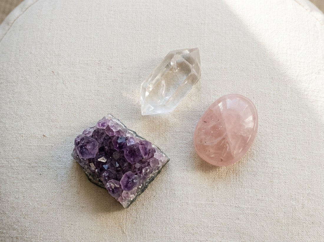 best crystals for meditation — a calm flat lay of amethyst, clear quartz, and rose quartz on a meditation cushion